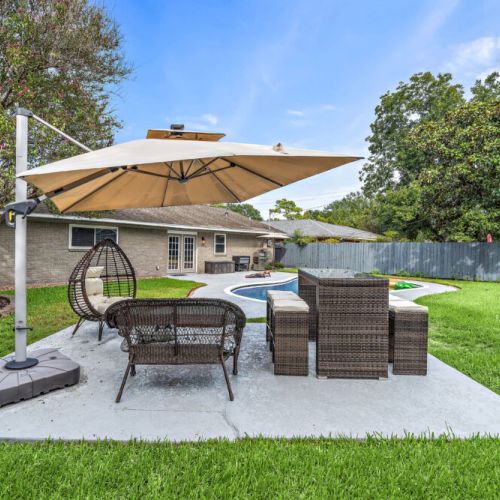 Backyard with grill, comfy sitting area, and cornhole set.