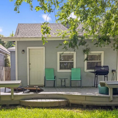 Inviting green private backyard with a deck, featuring a BBQ grill and a cornhole set!