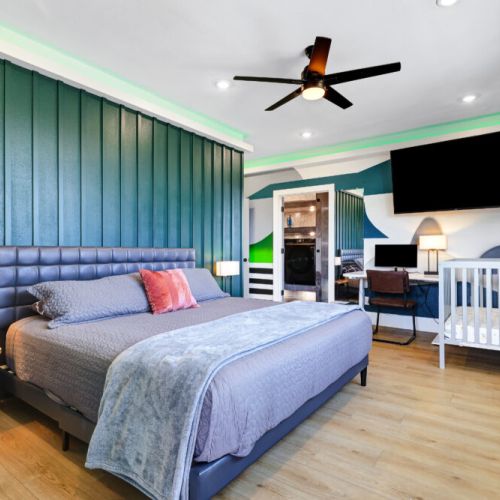 Primary bedroom with a king size bed, smart TV, attached bathroom, desk and electric fireplace