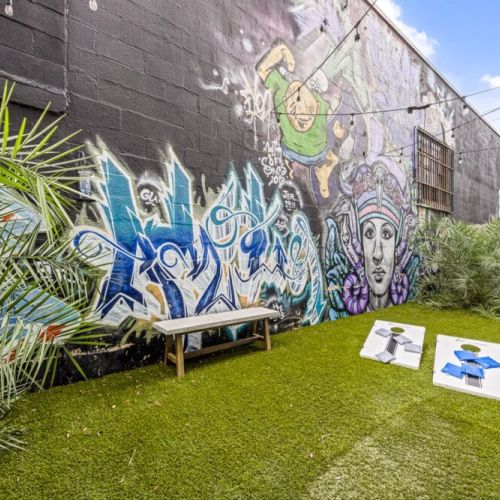 Enjoy a spacious outdoor backyard with vibrant murals, perfect for gathering, unwinding, and enjoying outdoor games like a fun, competitive cornhole tournament